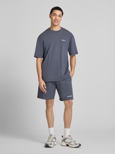 Męski model nosi Oversized Fit T-Shirt mit Logo-Stitching von Pegador, bawełna, krój oversized fit, okrągły dekolt, długość tyłu M: 71 cm, ciemnoszary, gładka tekstura, prosty krój, przód, widok całej sylwetki