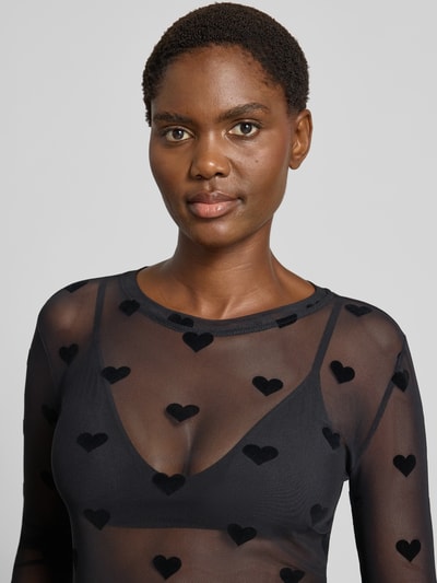 Frauenmodel trägt Slim Fit Langarmshirt mit Rundhalsausschnitt Modell 'LOVA' von VERO MODA, transparenter schwarzer Stoff mit samtigen Herzmotiven, Damen Langarmshirt, Nahaufnahme Oberkörper.