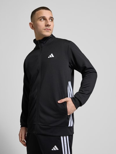 Männermodel trägt Regular Fit Trainingsjacke mit Label Print von adidas Training, Optik: Unifarben, Reißverschluss, Ganzkörperansicht von vorne.