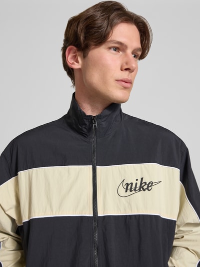 Männermodel trägt Trainingsjacke mit Logo und Reißverschluss von Nike in Regular-Fit mit Stehkragen, Nahaufnahme Oberkörper.