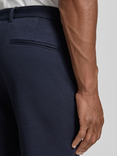 Mężczyzna nosi Slim Fit Hose mit Viskose-Anteil in verkürzter Passform von Lindbergh, granatowa mieszanka wiskozy, wpuszczana kieszeń z tyłu, długość wewnętrzna nogawki 72 cm, szerokość w rozmiarze M: 42 cm. Detailaufnahme dłoni i tylnej kieszeni.
