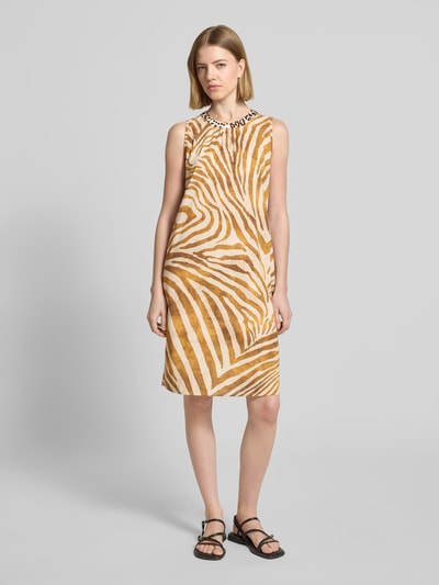Frauenmodel trägt Knielanges Kleid mit rückseitigem Schlüsselloch-Ausschnitt von Emily Van den Bergh, beige-braunes Zebra-Muster, reine Baumwolle, gerader Schnitt, Rundhalsausschnitt, Knopfverschluss hinten, Ganzkörperansicht von vorne.