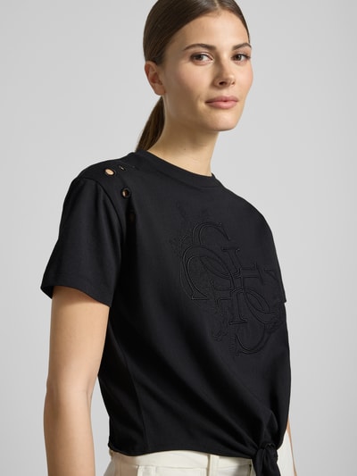 Frauenmodel trägt Regular Fit T-Shirt mit Lochmuster von Guess aus reiner Baumwolle, Logo-Stitching, Rundhalsausschnitt, schwarze Farbe, Nahaufnahme Oberkörper.