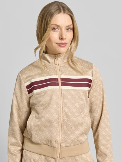 Frauenmodel trägt Regular Fit Sweatjacke mit Allover-Logo-Print Modell 'Jacquard' von Guess Activewear in Beige mit Reißverschluss, Nahaufnahme Oberkörper.