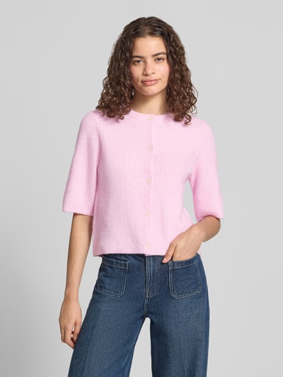 Frauenmodel trägt Boxy Fit Strickjacke aus Rippstrick Modell 'SILLY' von PIECES in rosa Melange, kurzarm, einreihige Knopfleiste, Ganzkörperansicht von vorne.