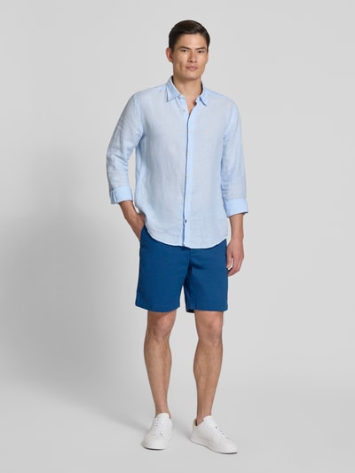 Männermodel trägt Chinoshorts aus Baumwoll-Mix Modell 'DOVER' von Tommy Hilfiger in Blau, Regular Fit, seitliche Eingrifftaschen, Ganzkörperansicht von vorne.