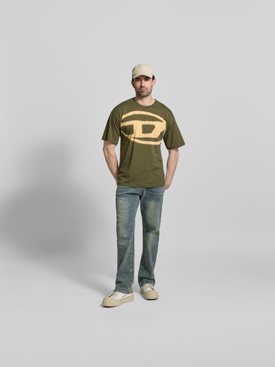 Männermodel trägt Regular Fit T-Shirt mit Logo-Print von Diesel, grün-beige, reine Baumwolle, Rundhalsausschnitt, Kurzarm, Ganzkörperansicht von vorne.