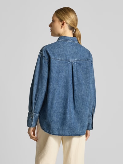 Männermodel trägt Loose Fit Jeansbluse aus reiner Baumwolle von s.Oliver RED LABEL, tkanina stylizowana na denim, krój loose fit, kołnierzyk koszulowy, aplikacja z napisem, pas na plecach z kontrafałdą, dekolt w serek, ukryta listwa guzikowa, długi rękaw z mankietem, wykończenie materiału: splot twill, 100% bawełna. Ganzkörperansicht Rückansicht.