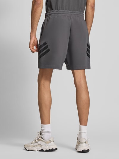 Männermodel trägt Regular Fit Sweatshorts mit Baumwoll-Anteil von adidas Sportswear, Optik: Unifarben, Materialverarbeitung: Sweat, mit Logo-Print, elastischem Bundabschluss mit Tunnelzug und seitlichen Eingrifftaschen, Farbe Grau, Ganzkörperansicht Rückansicht.