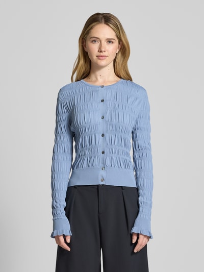 Frauenmodel trägt Cardigan mit Smok-Details und Rundhalsausschnitt von Scotch & Soda, Slim Fit, Knopfleiste, Farbe Hellblau, Ganzkörperansicht von vorne.