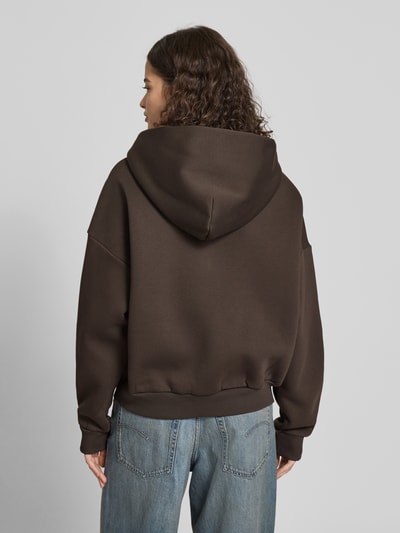 Frauenmodel trägt Sweatjacke mit Logo und Känguru-Tasche von Review, mieszanka bawełny, krój relaxed fit, kaptur, zamek błyskawiczny, kieszeń kangurka, logo, Ganzkörperansicht Rückansicht