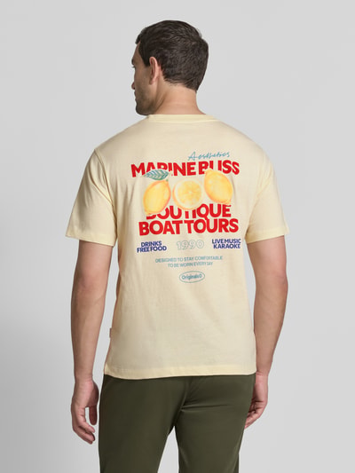 Männermodel trägt Herren T-Shirt von JACK & JONES aus Reiner Baumwolle, Straight Fit, Modell 'RIVIERA VINTAGE POSTER', Logo-Print, Rückseitiger Motiv- und Statement-Print, Rundhalsausschnitt, Pastellgelb mit mehrfarbigem Rückenprint, Rückenlänge bei Größe M 67 cm, Ganzkörperansicht Rückansicht.