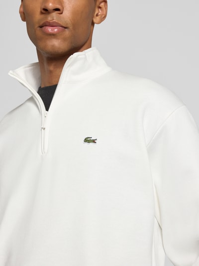 Männermodel trägt Regular Fit Troyer aus Baumwoll-Mix von Lacoste in Weiß mit Reißverschluss, dezentes Logo, Nahaufnahme Oberkörper. Herren Troyer von Lacoste