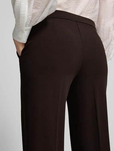 Männermodel trägt spodnie z szerokimi nogawkami z wpuszczanymi kieszeniami Wide Leg Hose mit Eingrifftaschen Modell 'Hillda' von Stehmann, damskie spodnie o szerokim kroju, kolor ciemnobrązowy, gładka tekstura, detal z tyłu, damska moda, Ganzkörperansicht Rückansicht, kontekst: damskie weite spodnie od Stehmann