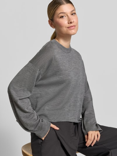 Frauenmodel trägt Strickpullover aus Schurwolle Modell 'MALESE' von DRYKORN in Grau, entspannter Sitz, reiner Wollstoff, Ganzkörperansicht von vorne.