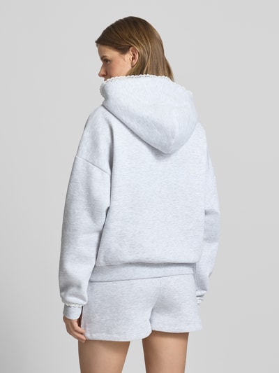 Frauenmodel trägt Hoodie mit Spitzenkanten an Kapuze, Känguru-Tasche und Ärmelbund von Review, Material-Mix mit Baumwoll-Anteil, Relaxed-Fit, Label-Stitching, hellgrau meliert, strukturierte Oberfläche, Ganzkörperansicht Rückansicht.
