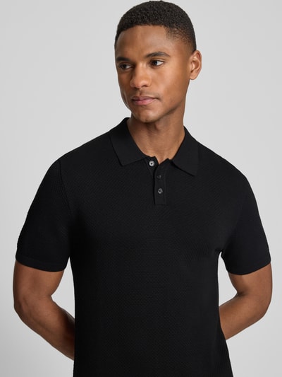 Männermodel trägt Slim Fit Poloshirt Modell 'Triton' von Drykorn in Schwarz, Reine Baumwolle, Polokragen, Strukturmuster, Nahaufnahme Oberkörper.