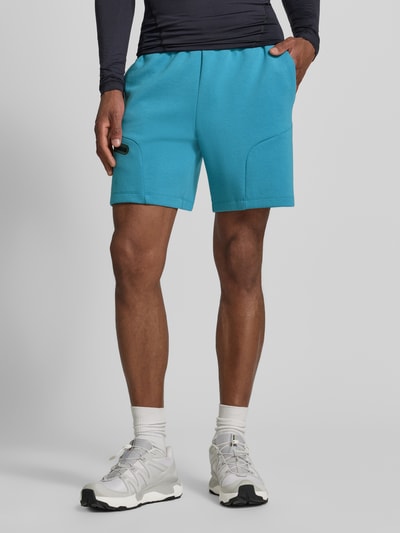Męski model nosi szorty z Reißverschlusstasche od Under Armour, mieszanka bawełny, krój regular fit, logo, pas elastyczny, szerokość w rozmiarze M: 39 cm, długość wewnętrzna nogawki w rozmiarze M: 18 cm, kolor turkusowy, gładka faktura, widok całej sylwetki z przodu.