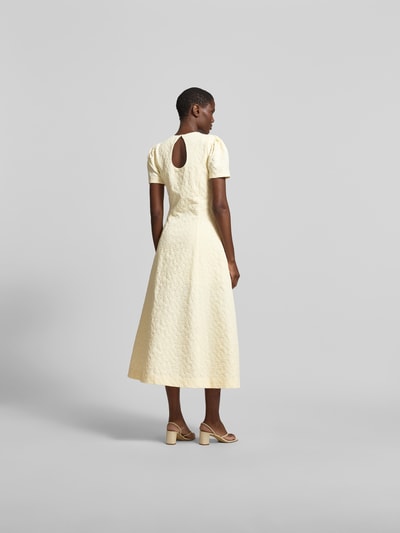 Frauenmodel trägt Midikleid mit floralem Allover-Detail von ROTATE, hellgelb, Elastischer-Material-Mix, A-Linie, taillierte Passform, kurzärmelig, strukturierte Oberfläche, Ganzkörperansicht Rückansicht. Gesamtlänge 128 cm, Brustweite 41 cm, Ärmellänge 12 cm.