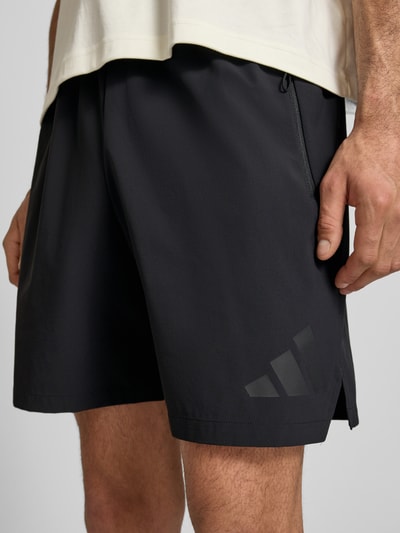 Männermodel trägt Regular Fit Shorts mit Tunnelzug von adidas Sportswear, Optik: Unifarben, Logo-Print, Kontraststreifen, seitliche Eingrifftaschen, Bundabschluss: elastisch mit Tunnelzug, Nahaufnahme Oberschenkel vorne.