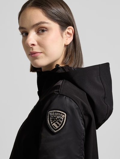 Frauenmodel trägt Regular Fit Jacke mit Logo-Detail Modell 'Marcela' von Blauer Usa, Kapuze, Eingrifftaschen, Schwarz, Detailaufnahme Schulter, Rückenlänge 60 cm, Schulterbreite 43 cm, Brustweite 47 cm, Ärmellänge 59 cm bei Größe S.