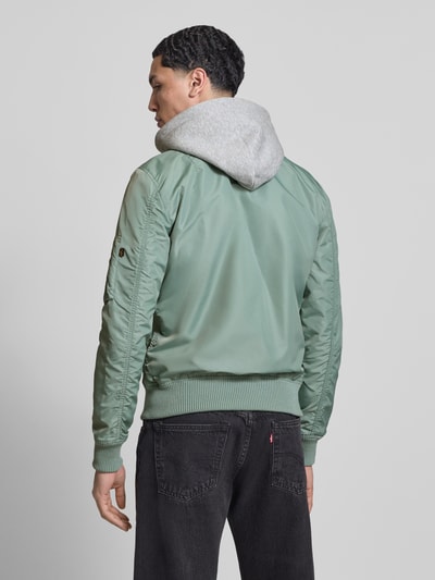 Männermodel trägt mintgrünen blouson mit logohanger Modell 'MA-1 TT' von Alpha Industries, capuchon van sweatstof, los model, mouwzak, labelpatch, elastische boorden; context: heren blouson, maat M ruglengte 69 cm, schouderbreedte 46 cm, borstwijdte 54 cm, mouwlengte 67 cm; Ganzkörperansicht Rückansicht.