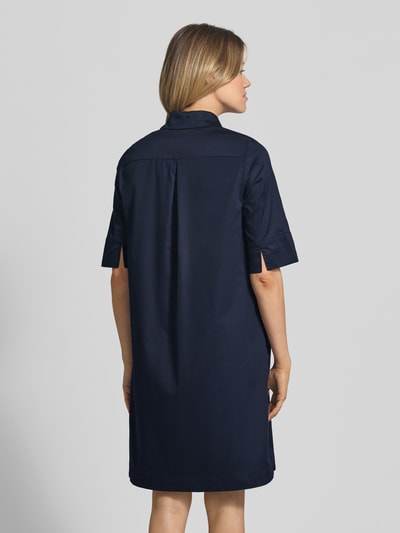 Frauenmodel trägt knielanges Hemdblusenkleid mit Eingrifftaschen von Christian Berg Woman aus dunkelblauer Baumwolle, Ganzkörperansicht Rückansicht.