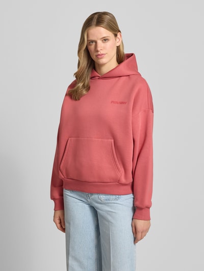 Frauenmodel trägt Hoodie mit Logo und Känguru-Tasche von REVIEW in Rosa aus Baumwoll-Mix, Relaxed-Fit, Ganzkörperansicht von vorne.