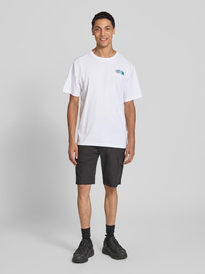 Męski model nosi Relaxed Fit T-Shirt mit Logo-Print von The North Face, biała bawełna, okrągły dekolt, długość tyłu w rozmiarze M: 71 cm, ganzkörperansicht von vorne.