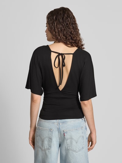 Frauenmodel trägt Bluse aus Viskose-Mix mit V-Ausschnitt von Gina Tricot in Schwarz, taillierte Passform, Halbarm, Ganzkörperansicht Rückansicht.