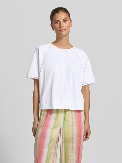 Kobiece model nosi Relaxed Fit T-Shirt mit Rundhalsausschnitt von Marc Cain, damski t-shirt z bawełny, ozdobne szwy, długość tyłu 52 cm w rozmiarze 36, kolory białe i pastelowe, gładka tekstura, Ganzkörperansicht von vorne.