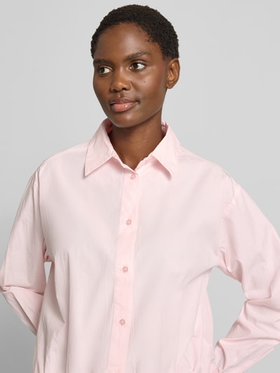 Frauenmodel trägt Regular Fit Hemdbluse aus reiner Baumwolle Modell 'Emmana' von Neo Noir in zartem Rosa, glatte Textur, Nahaufnahme Oberkörper. Rückenlänge 53 cm, Ärmel 64 cm, Hemdblusenkragen, durchgehende Knopfleiste, 1-Knopf-Manschetten, elastischer Saum.