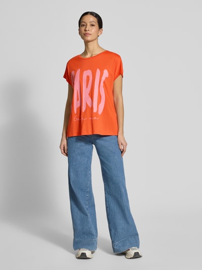 Frauenmodel trägt Oversized Fit T-Shirt aus Viskose-Mix von Smith and Soul, orange mit rosa Motiv-Print, Baumwoll-Viskose-Mix, Rundhalsausschnitt, Rückenlänge 62 cm, Ganzkörperansicht von vorne.