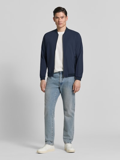 Männermodel trägt dunkelblaue Regular Fit Jacke mit Stehkragen Modell 'Campo' von SCANDINAVIAN EDITION, glatte Textur, Ganzkörperansicht von vorne, Kontext: Herren Jacke mit Zweiwege-Reißverschluss, Eingrifftaschen mit Reißverschluss, elastische Abschlüsse, Rückenlänge bei Größe M 67 cm, Schulterbreite 44 cm, Brustweite 51 cm, Ärmellänge 64 cm.