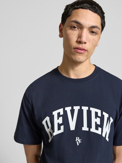 Männermodel trägt T-Shirt mit Label-Print und Rundhalsausschnitt von REVIEW in Dunkelblau, reine Baumwolle, Regular Fit, Nahaufnahme Oberkörper.