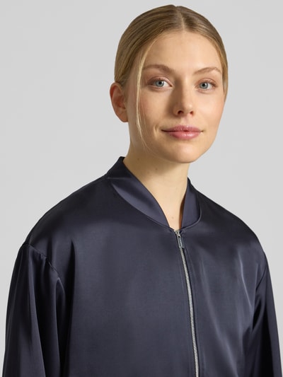 Frauenmodel trägt Blouson mit Stehkragen und Reißverschluss von Comma, dunkler Material-Mix mit Viskose-Anteil, Nahaufnahme Oberkörper. Regular-Fit, Rückenlänge 52 cm, Brustweite 50 cm, Ärmellänge 57 cm, Größe 36.