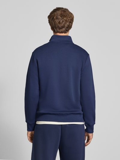 Mężczyzna nosi Sweatshirt aus reiner Baumwolle od REVIEW, granatowy kolor, wyhaftowane logo, kołnierz zapinany, prążkowane wykończenia, luźny krój, Długość tyłu w rozmiarze M: 68 cm, Długość rękawów w rozmiarze M: 66 cm, widok całej sylwetki z tyłu.