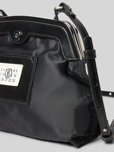 Produktfoto, Pochette mit Magnetverschluss von MM6 Maison Margiela mit glattem Design, Label-Patch, Motiv-Print und verstellbarem Schulterriemen, Hauptfach, schwarz, Maße: 25 cm Breite, 20 cm Länge, 9 cm Tiefe.