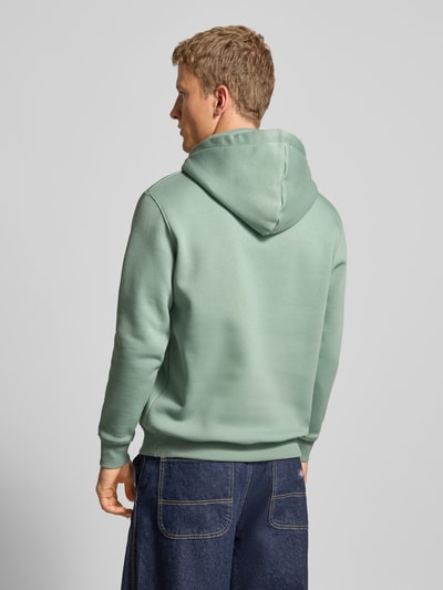 Męski model nosi Hoodie mit Logo und Känguru-Tasche von Alpha Industries, mieszanka bawełny, krój regular fit, długość tyłu 69 cm, długość rękawów 64 cm, kolor miętowy, widok od tyłu, całkowity.