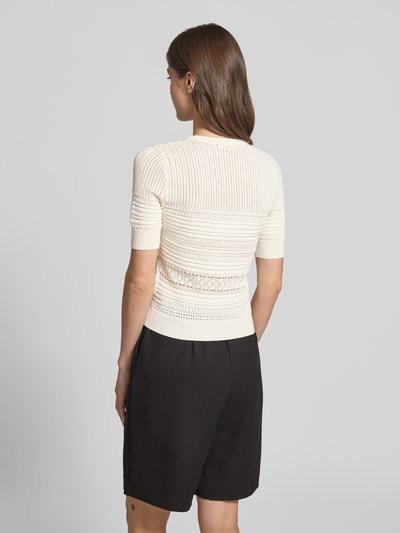 Frauenmodel trägt T-Shirt in Strick-Optik mit Rundhalsausschnitt von Guess in creme, feine Rippenstruktur, gerippte Abschlüsse, Ganzkörperansicht Rückansicht.