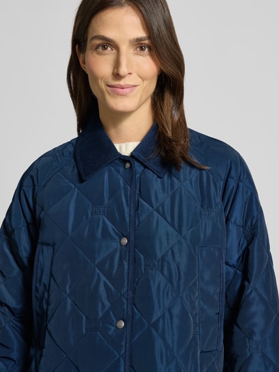 Vrouwenmodel draagt Regular Fit Steppmantel met Logo-Details van Tommy Hilfiger, donkerblauw, gewatteerde textuur, lange mouwen, kraag met cord, drukknopen, borst- en klepzakken, logo-appliek, Nahaufnahme oberkörper.