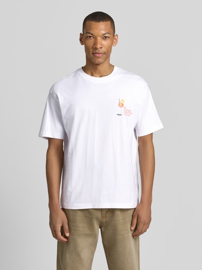 Männermodel trägt T-Shirt mit rückseitigem Motiv-Print von MCNEAL in Weiß, gerader Schnitt, Rundhals, Statement-Print, Ganzkörperansicht von vorne.
