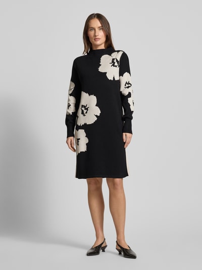 Vrouwenmodel draagt Relaxed Fit jurk uit viscosemix in tricotlook van Betty Barclay, zwart met bloemenmotief, knielengte, opstaande kraag, lang mouwen, elastische mouwboorden, voorkant volledig zichtbaar, knielange ruglengte maat 36, borstwijdte 49 cm, mouwlengte 70 cm; Ganzkörperansicht von voren.