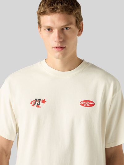 Männermodel trägt Relaxed Fit T-Shirt aus reiner Baumwolle von Levi's®, cremeweiß mit roten und schwarzen Prints, Nahaufnahme Oberkörper.