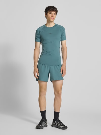 Männermodel trägt T-Shirt mit Logo-Print und Rundhalsausschnitt von NIKE TRAINING in Türkis, Slim-Fit, Raglanärmel, Ganzkörperansicht von vorne. Rückenlänge bei Größe M: 72 cm.