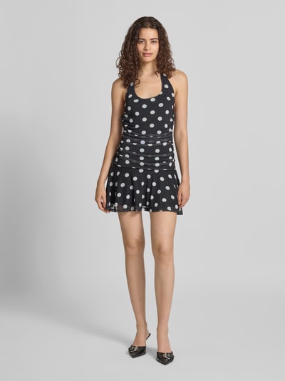 Frauenmodel trägt Neckholder-Minikleid im Allover-Look Modell 'DOTTIE' von NOISY MAY®, Slim Fit, schwarz-weißes Punktmuster, Ganzkörperansicht von vorne. Material-Mix mit Stretch-Anteil.