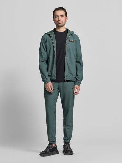 Männermodel trägt Regular Fit Sweatpants mit Strukturmuster von EA7 Emporio Armani in Grün, Elastischer-Material-Mix, Eingrifftaschen, Elastischer Bund mit Tunnelzug, Herren, Ganzkörperansicht von vorne.