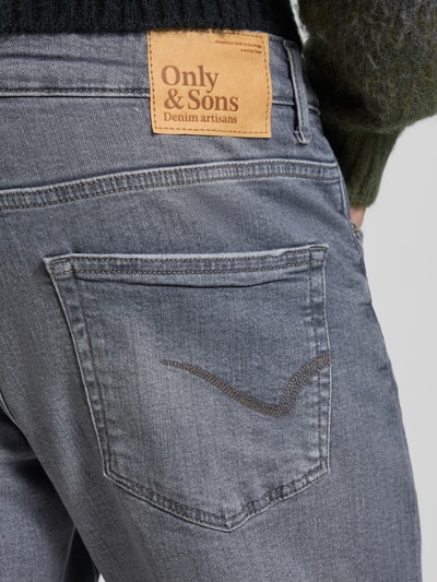 Mężczyznamodel nosi Regular Fit Jeans aus Baumwoll-Mix von Only & Sons, bawełniany denim, szary, label patch, label stitching, 5 kieszeni, detal tylnej kieszeni, krój regular fit, zdjęcie zbliżeniowe tyłu.