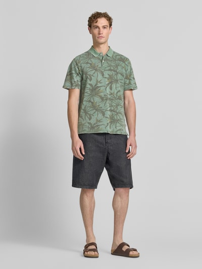Męski model nosi Regular Fit Poloshirt mit floralem Allover-Print Modell 'Hawaii' od JACK & JONES Premium, zielone odcienie, bawełna, krótki rękaw, widok całej sylwetki z przodu, kontekst: damska koszulka polo, krój regular fit, długość tyłu w rozmiarze M: 68 cm.