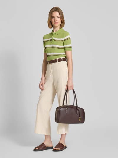 Frauenmodel trägt Slim Fit Poloshirt in Strick-Optik Modell 'Verdi' von Mango aus Material-Mix mit Baumwoll-Anteil, grün mit weißen Streifen, kurzärmelig, kombiniert mit heller Hose, Ganzkörperansicht von vorne.